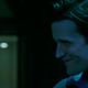 In a poorly lit room, Loxias Crown points a dropper at something and smiles